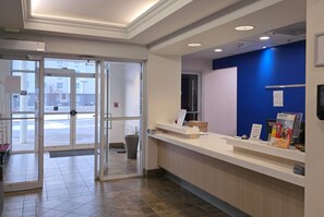 Zona de recepción con entrada por puerta de cristal, mostrador con folletos informativos y una pared azul de acento.