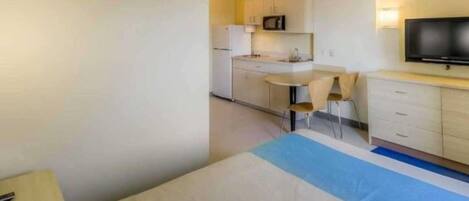 Una habitación de hotel compacta con cama, kitchenette pequeña, televisor y escritorio.
