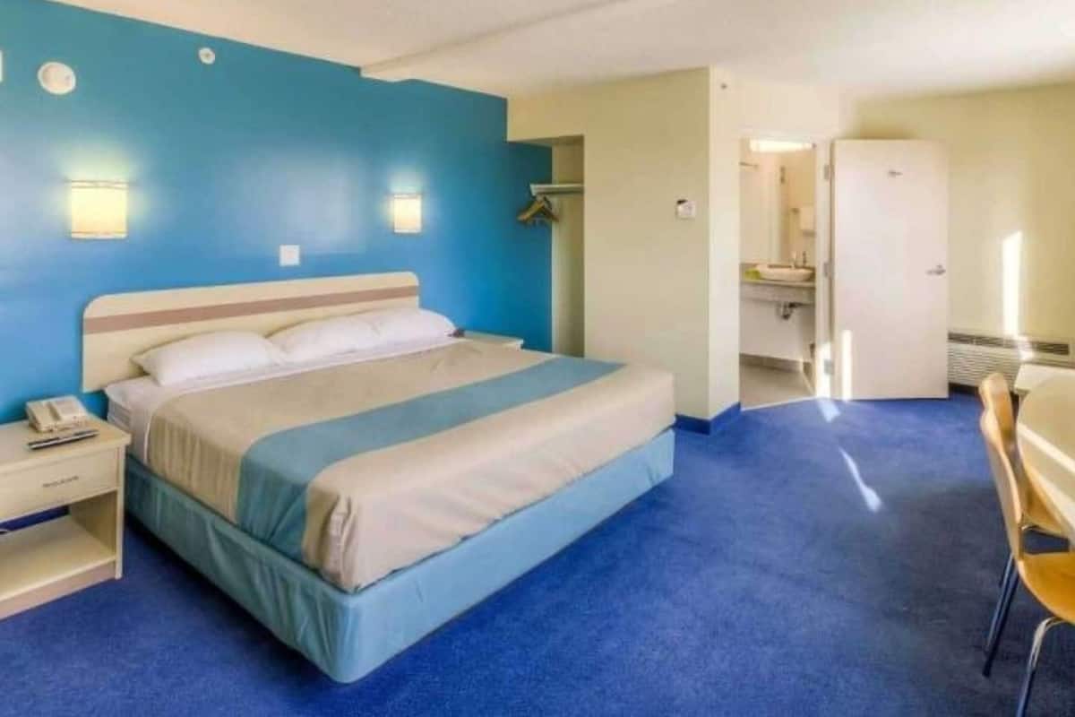 A single bed with a blue and white bedspread, a bedside table with a phone, and a chair.