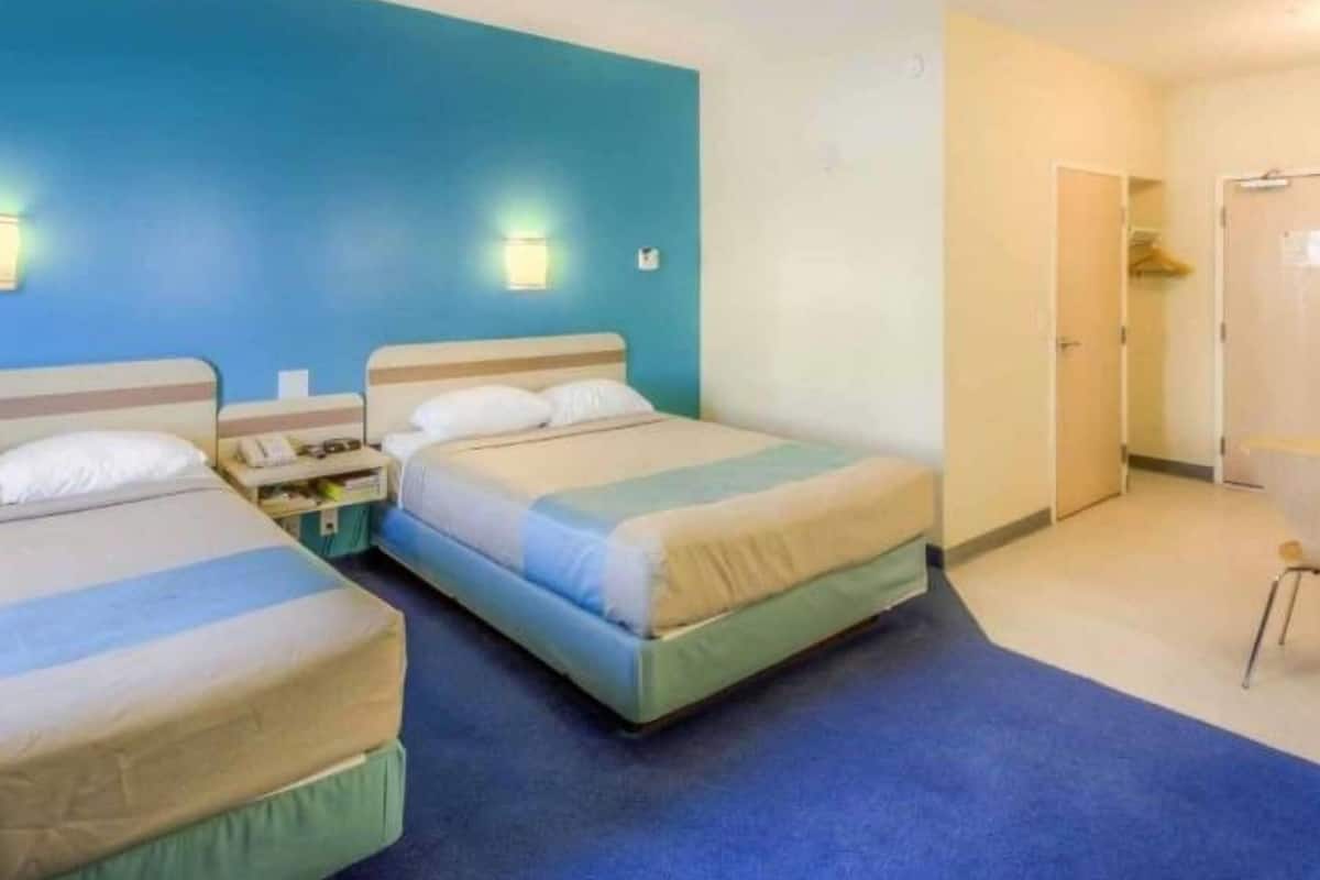 A hotel room with two beds, a blue wall, a door, and a small table with a phone.