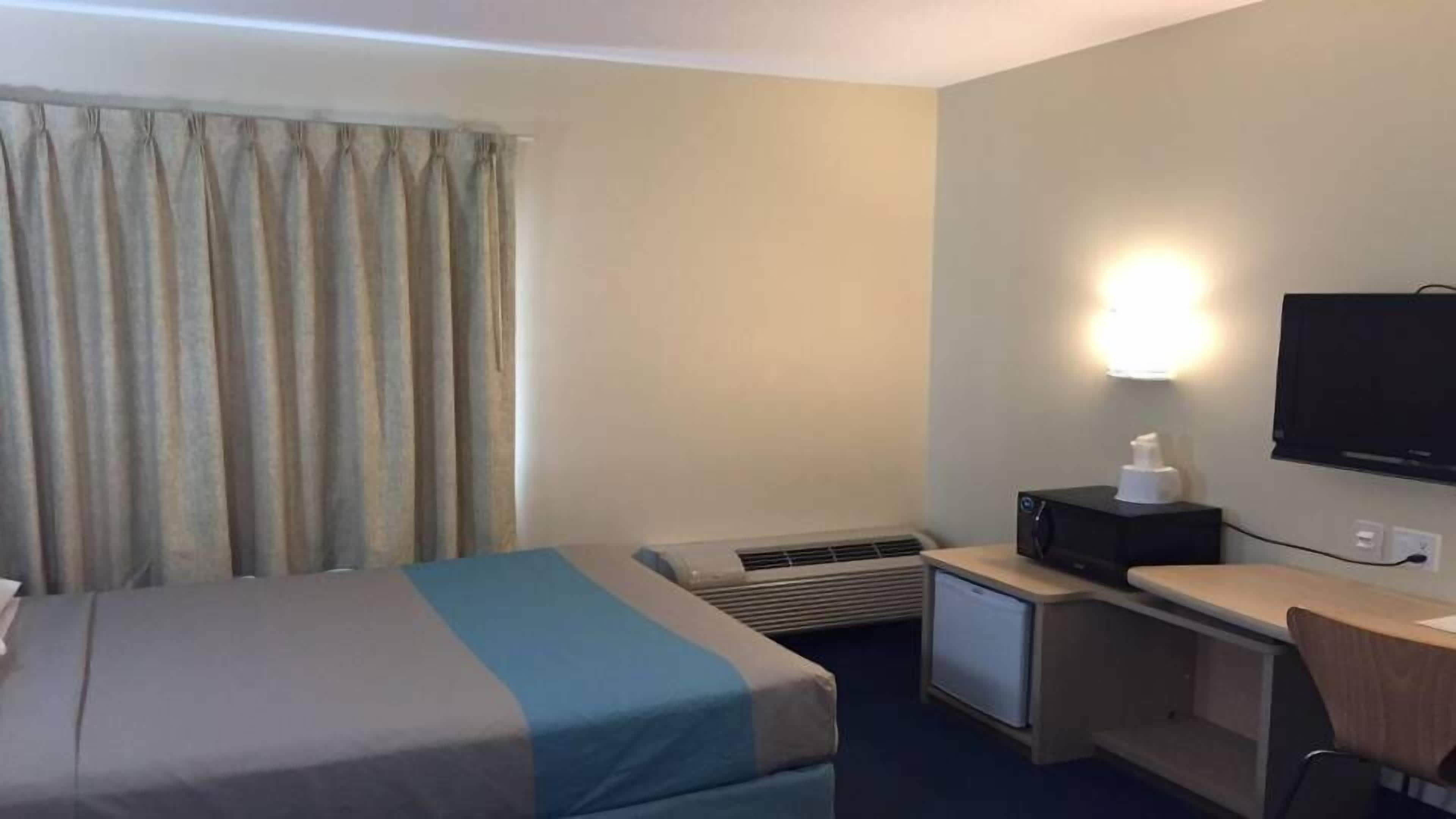Ett hotellrum med en säng, ett skrivbord, en tv och en värmare.