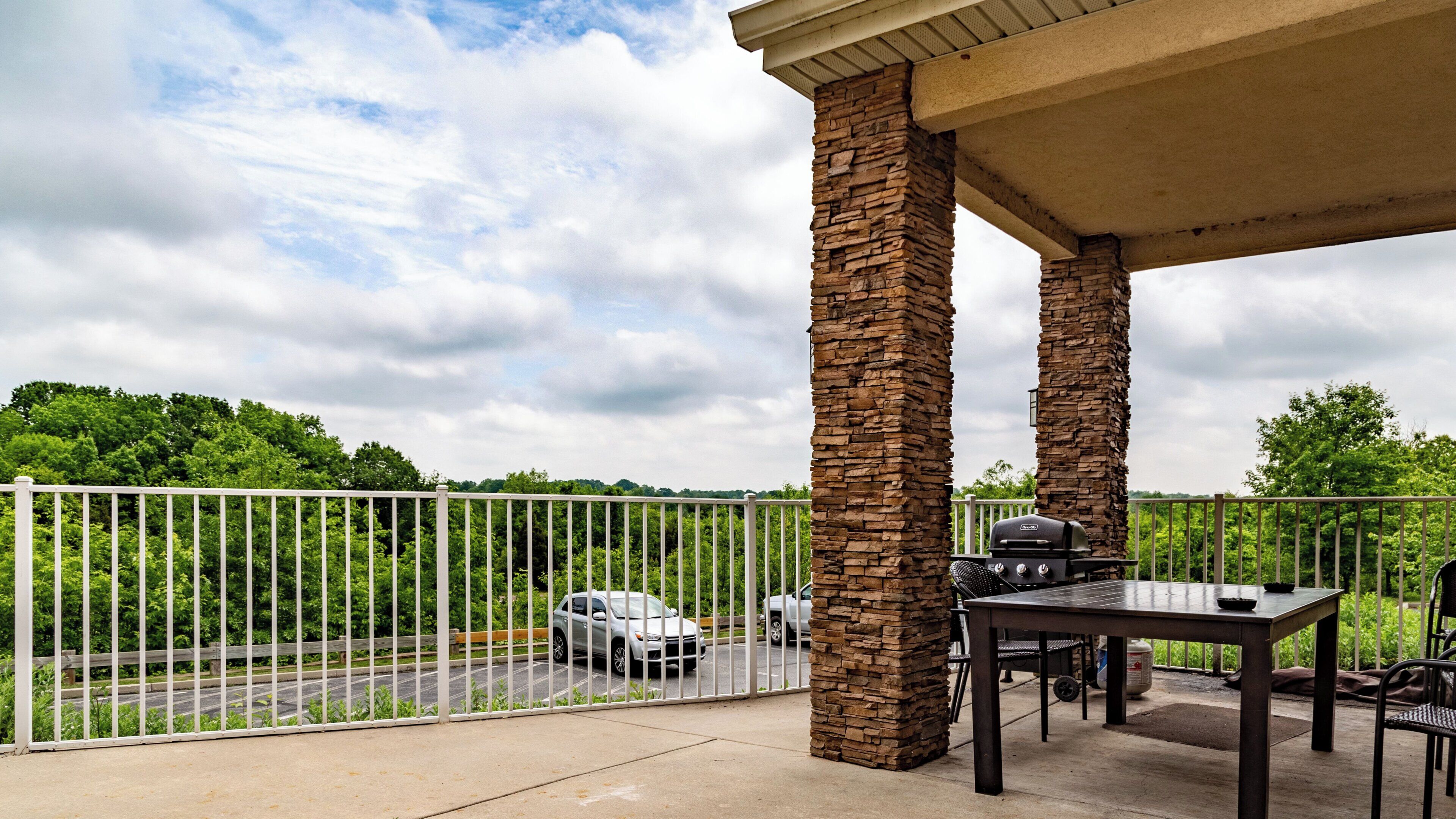 A covered outdoor area with stone pillars, a barbecue grill, and a table with chairs.