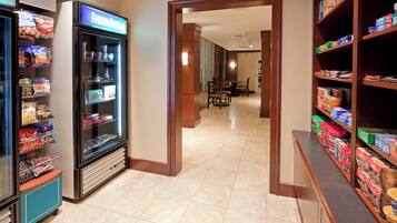 A hotel corridor with snack vending machines, a dining area, and shelves stocked with various food items.