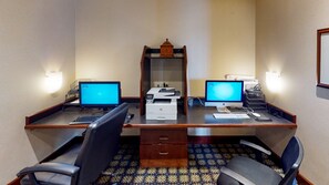 Une chambre d’hôtel équipée de deux bureaux, chacun comprenant un ordinateur de bureau, une imprimante et un clavier. Il y a deux chaises, une sur chaque bureau.