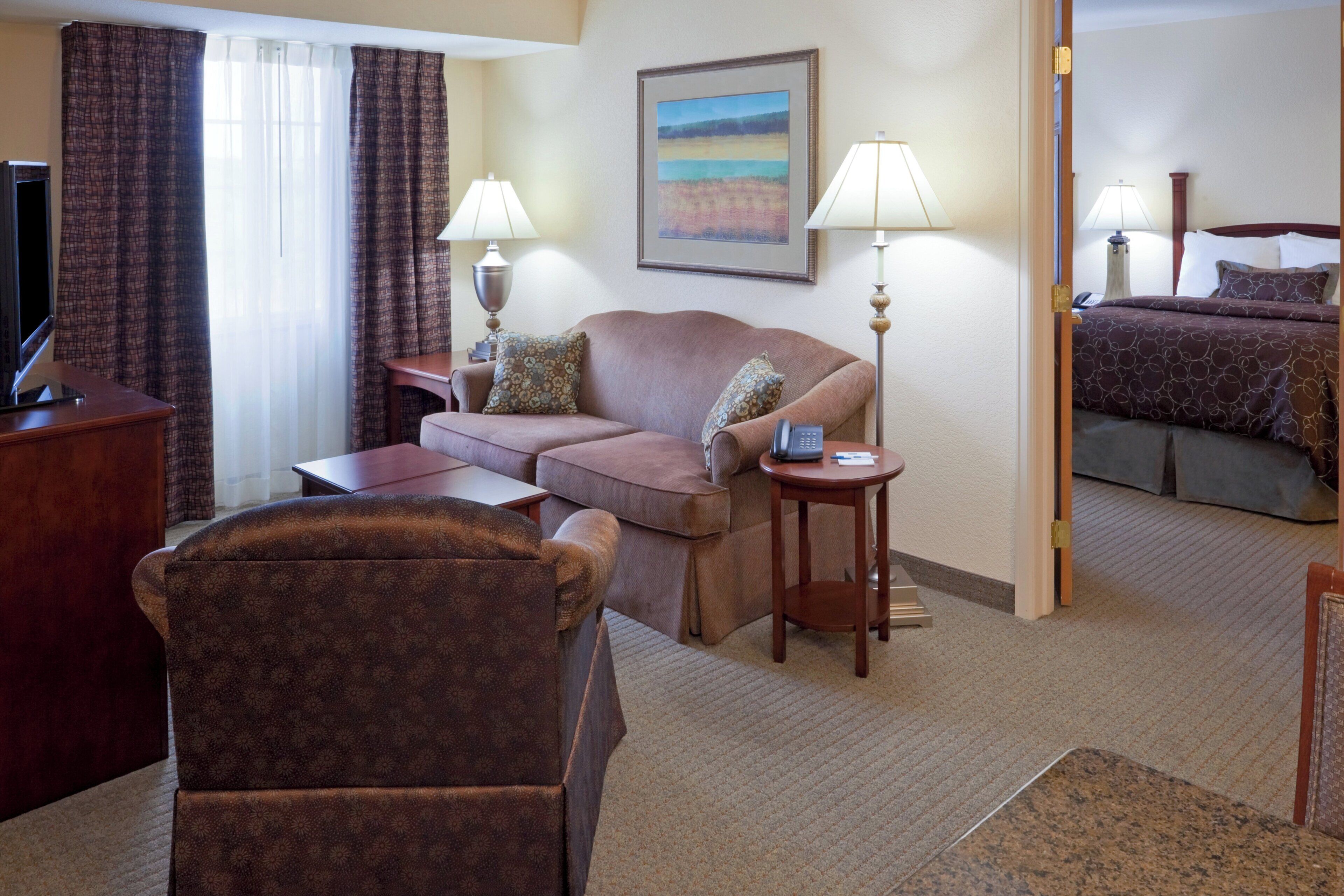 Habitación de hotel con sofá, sillón, escritorio, lámparas, un cuadro y cama.