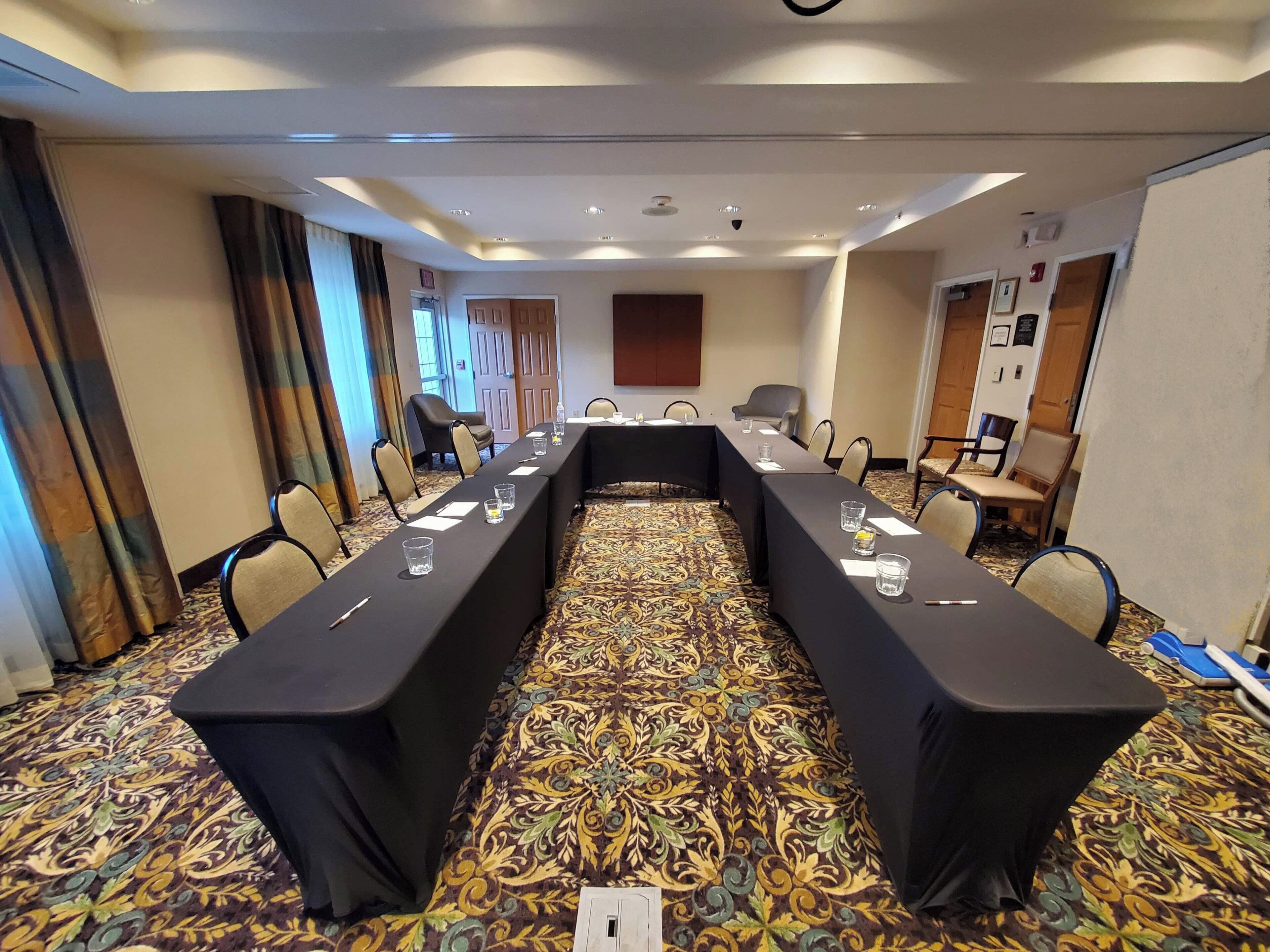 A conference room with a long table, chairs, and a patterned carpet.