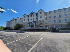 A multi-story hotel with a central entrance, a parking lot, and a clear blue sky. - Staybridge Suites Philadelphia Valley Forge 422 by IHG (Royersford)