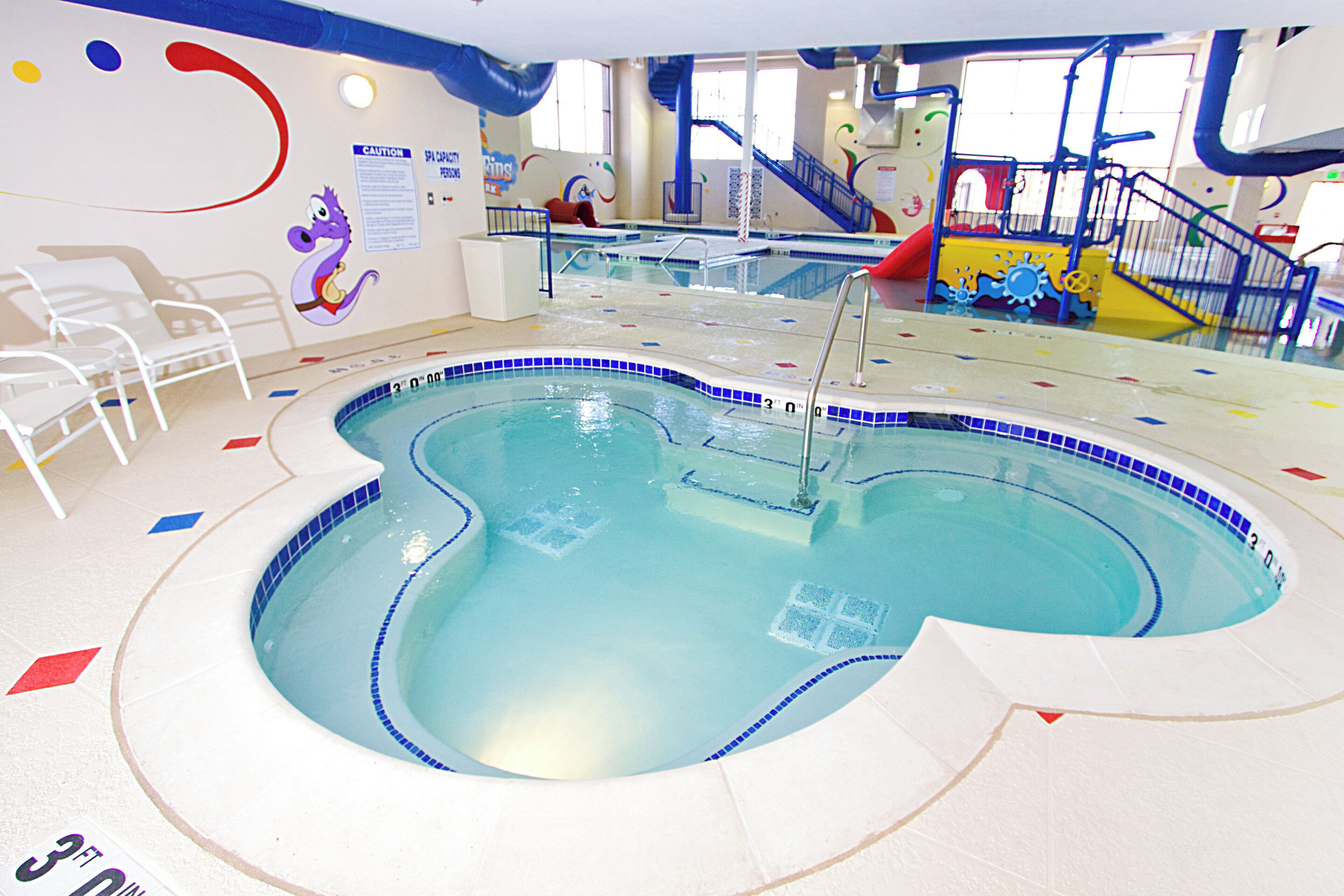 Una piscina interior con borde de azulejos azules, zona poco profunda y un tobogán.