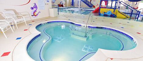 Una piscina interior con borde de azulejos azules, zona poco profunda y un tobogán.