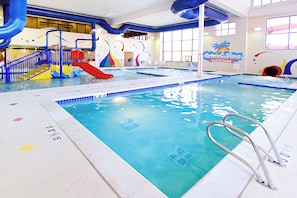 An indoor swimming pool with a red slide, blue and yellow play structures, and a sign for Grins & Fins Water Park.