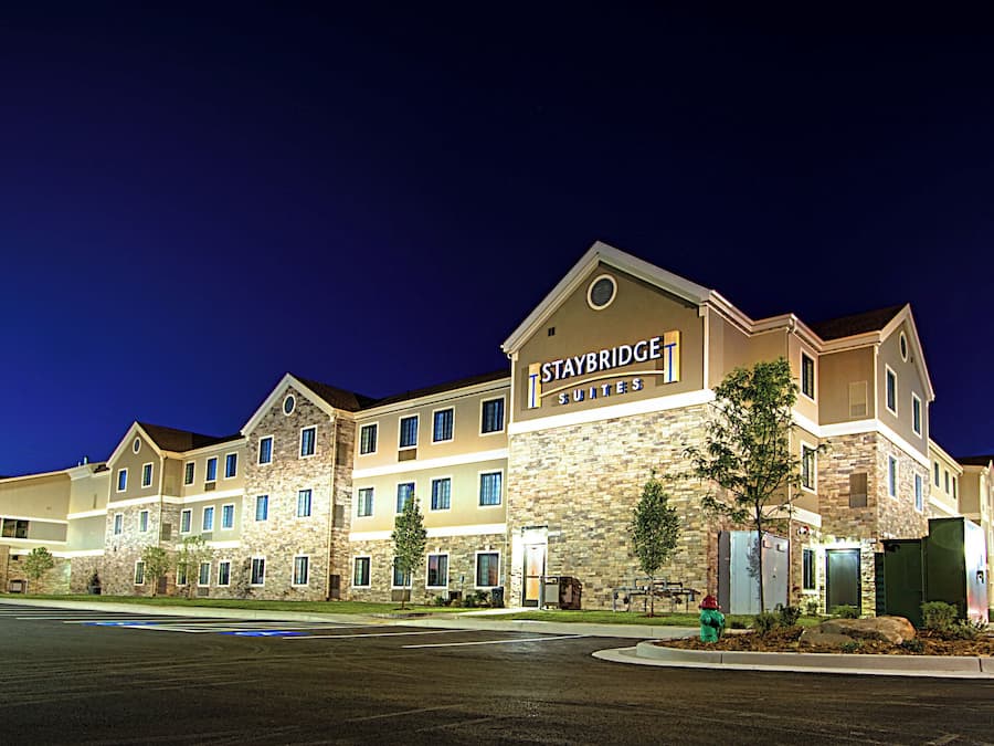 Un hotel Staybridge Suites con fachada de piedra, múltiples ventanas y una entrada bien iluminada.