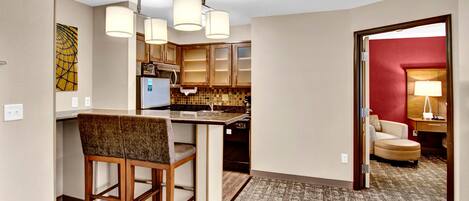 Habitación de hotel con kitchenette, zona de comedor con dos sillas, pared de acento roja y piso alfombrado.