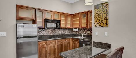 A modern kitchen with wooden cabinets, stainless steel appliances, a granite countertop, and pendant lighting.