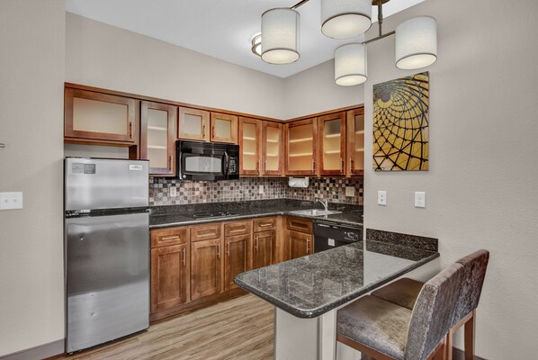 A modern kitchen with wooden cabinets, stainless steel appliances, a granite countertop, and pendant lighting.