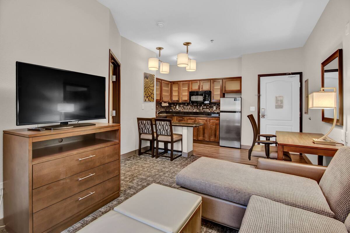 A compact living space with a sofa, TV, wooden cabinet, kitchenette, and dining area.