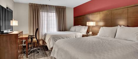 A hotel room with two beds, a desk, a chair, a TV, and a window with curtains.