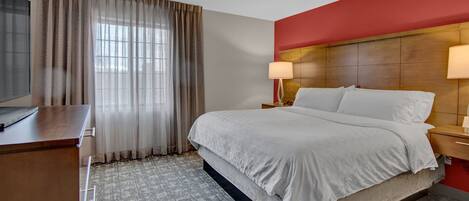 A hotel room with a large bed, a TV, a desk, and a window with curtains.