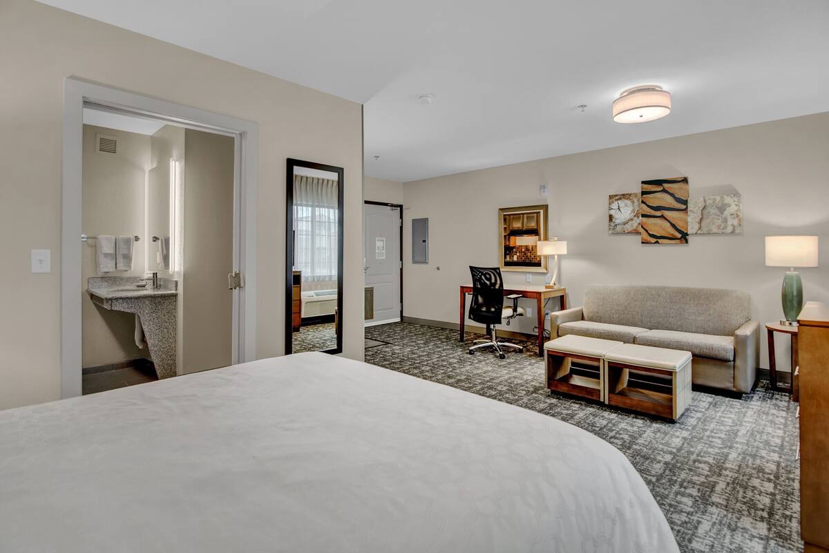A hotel room with a large bed, a desk with a chair, a sofa, and a small table with a lamp.