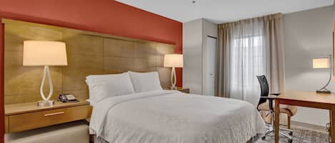 Une chambre d’hôtel avec un grand lit, deux tables de chevet avec des lampes, un bureau et une chaise.