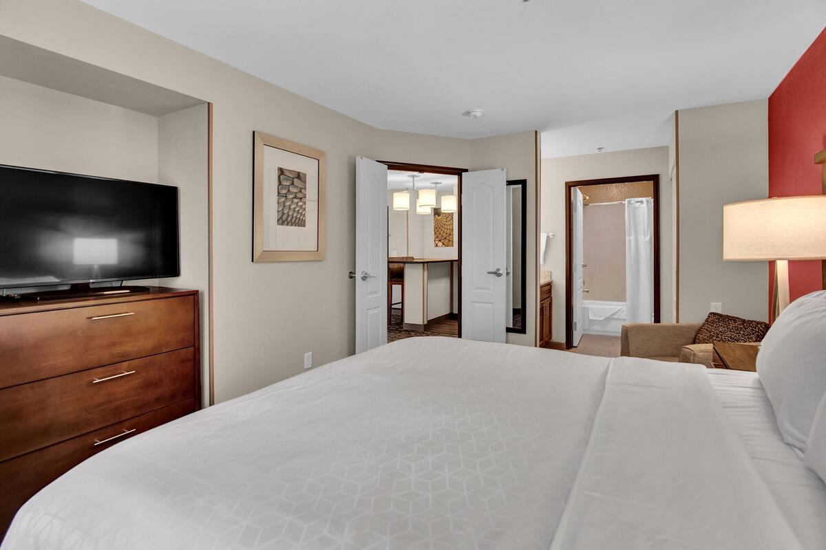 A hotel room with a large bed, a TV on a wooden dresser, and a bathroom visible through an open door.