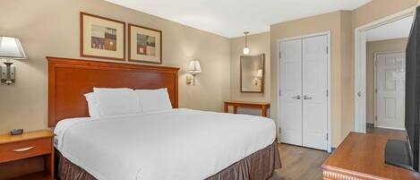 A hotel room with a large bed, bedside tables, a desk, a mirror, and two doors.