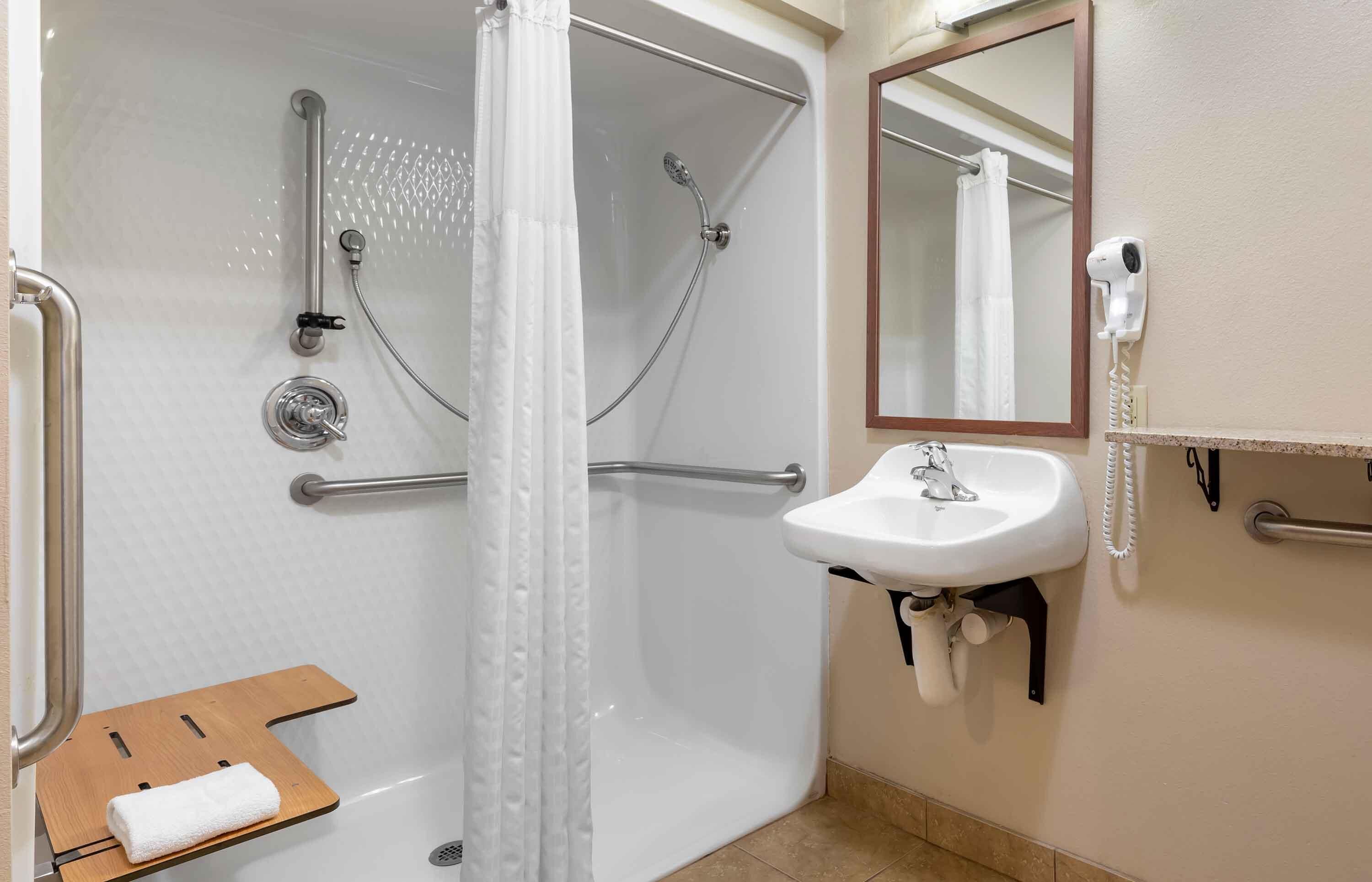Une douche avec une porte en verre, un lavabo blanc, un miroir et un porte-serviettes.