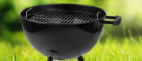 A black barbecue grill with a wire grate, set on a stand, in a grassy area.
