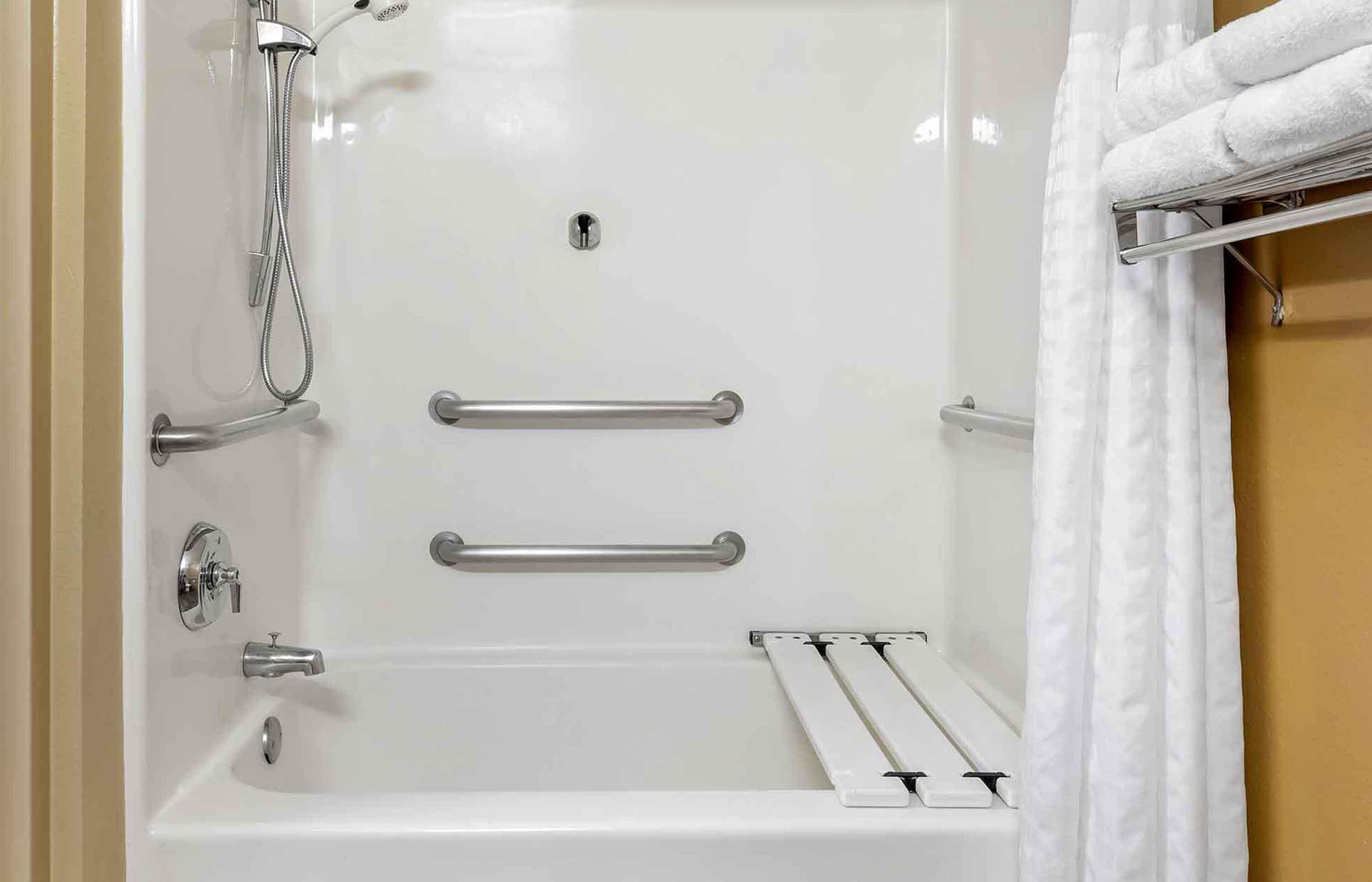 A white bathtub with a showerhead, grab bars, and a towel rack.
