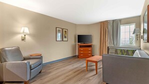 A hotel room with a sofa, a television, a small table, a cabinet, and a window with curtains.
