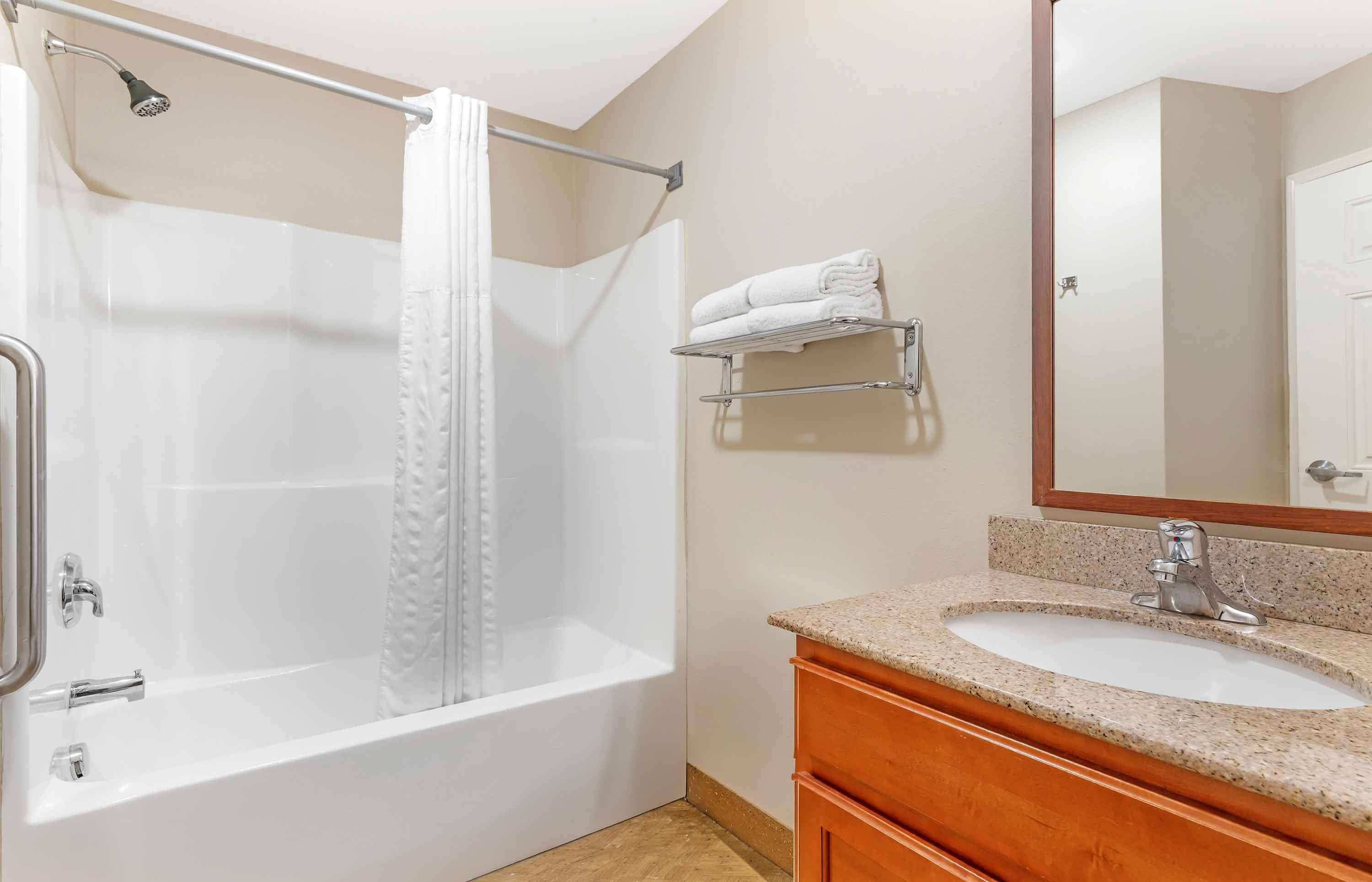 A bathroom with a bathtub, a sink, a mirror, and a towel rack.