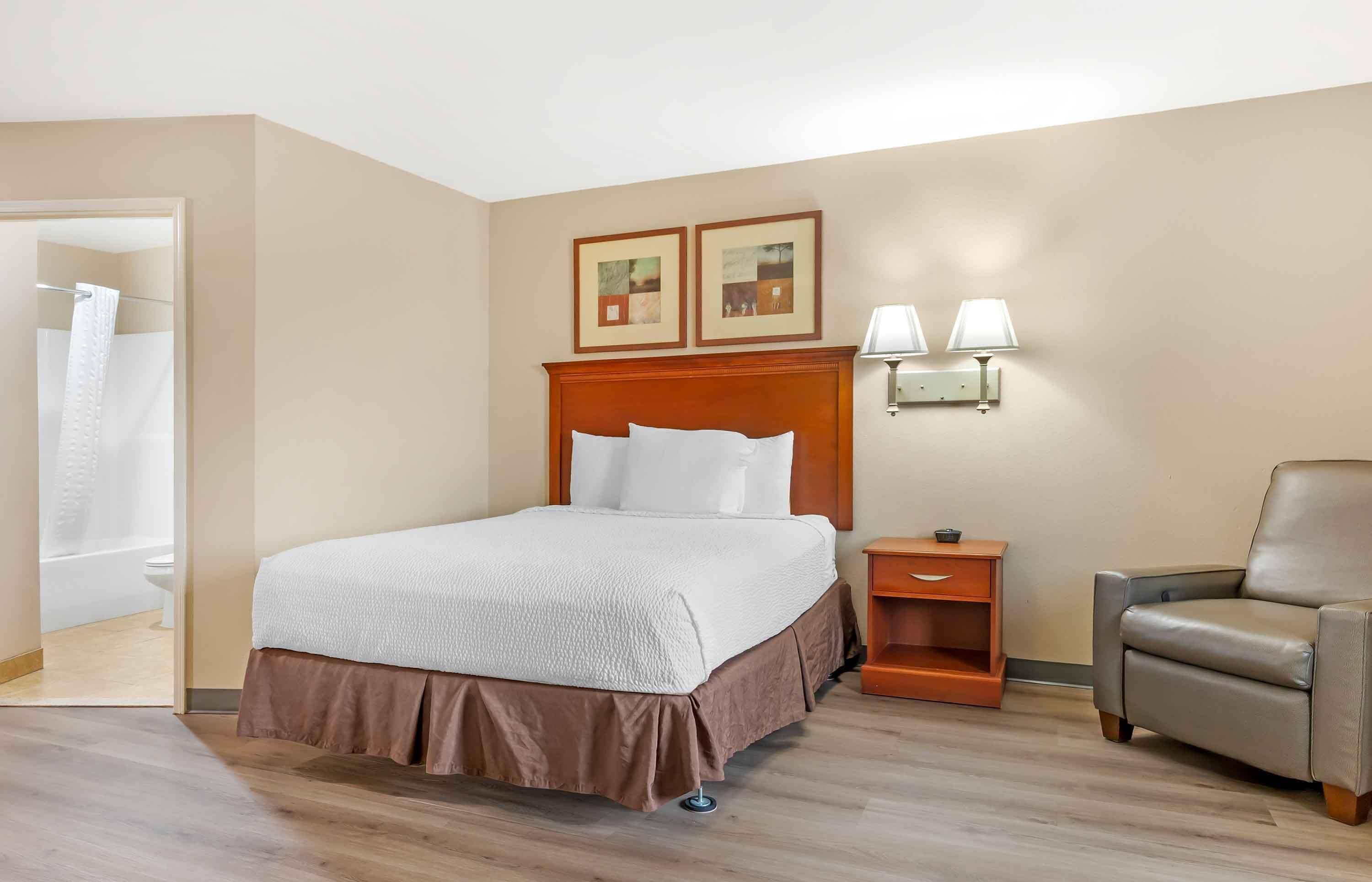 Una camera d'albergo con un letto, una sedia, un comodino e due lampade a parete.