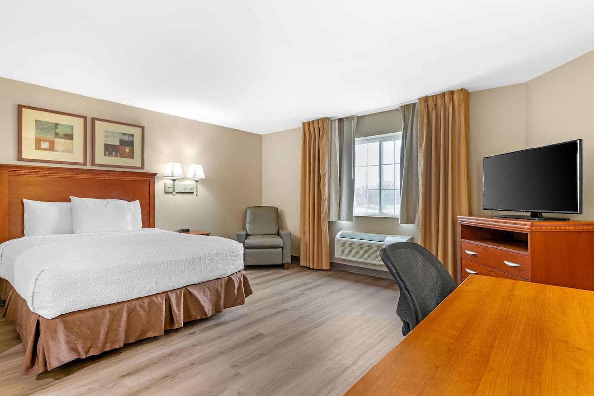 A hotel room with a bed, a desk, a television, a chair, and a window with curtains.
