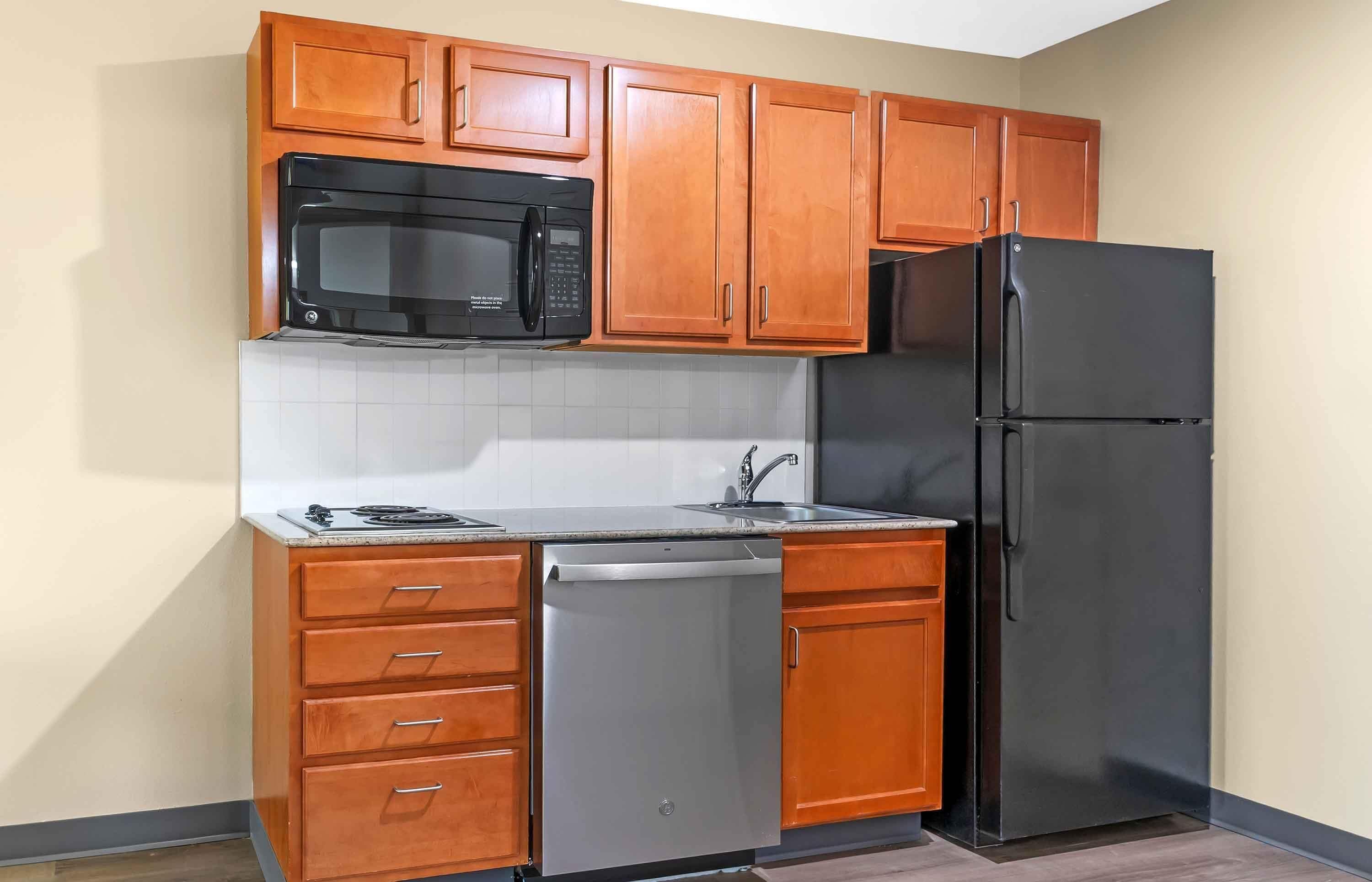 A compact kitchen with wooden cabinets, a black microwave, a black refrigerator, and a built-in dishwasher.