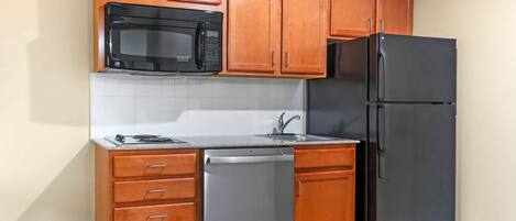 A compact kitchen with wooden cabinets, a black microwave, a black refrigerator, and a built-in dishwasher.