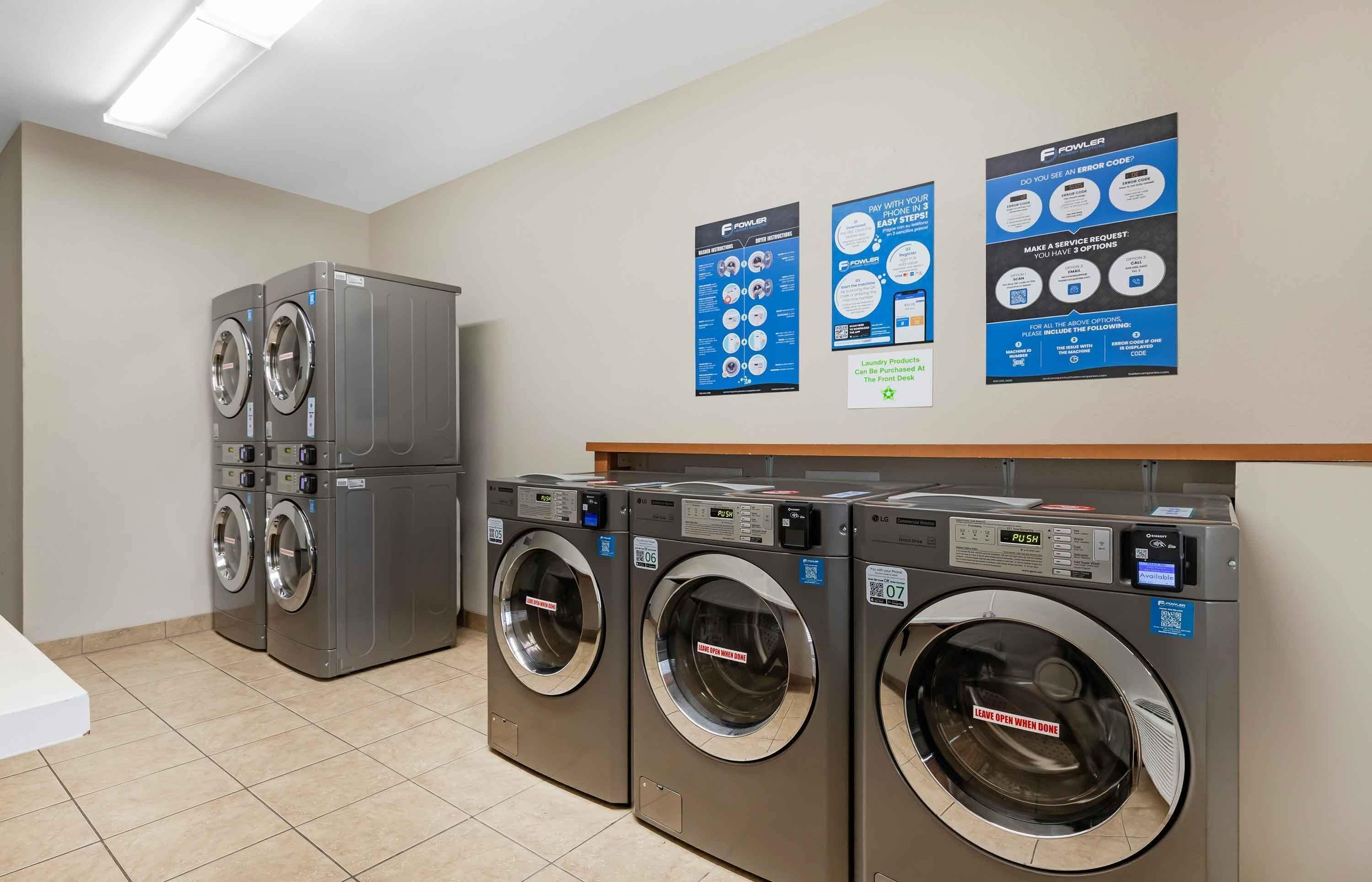 A laundry facility with multiple washing machines, a control panel, and informational posters on the wall.