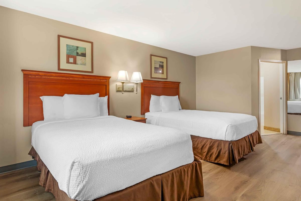 A hotel room with two beds, wooden headboards, a nightstand with lamps, and framed artwork on the walls.