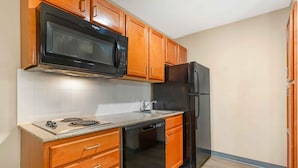 A kitchen with wooden cabinets, a black microwave, a black refrigerator, a dishwasher, and a tiled backsplash.
