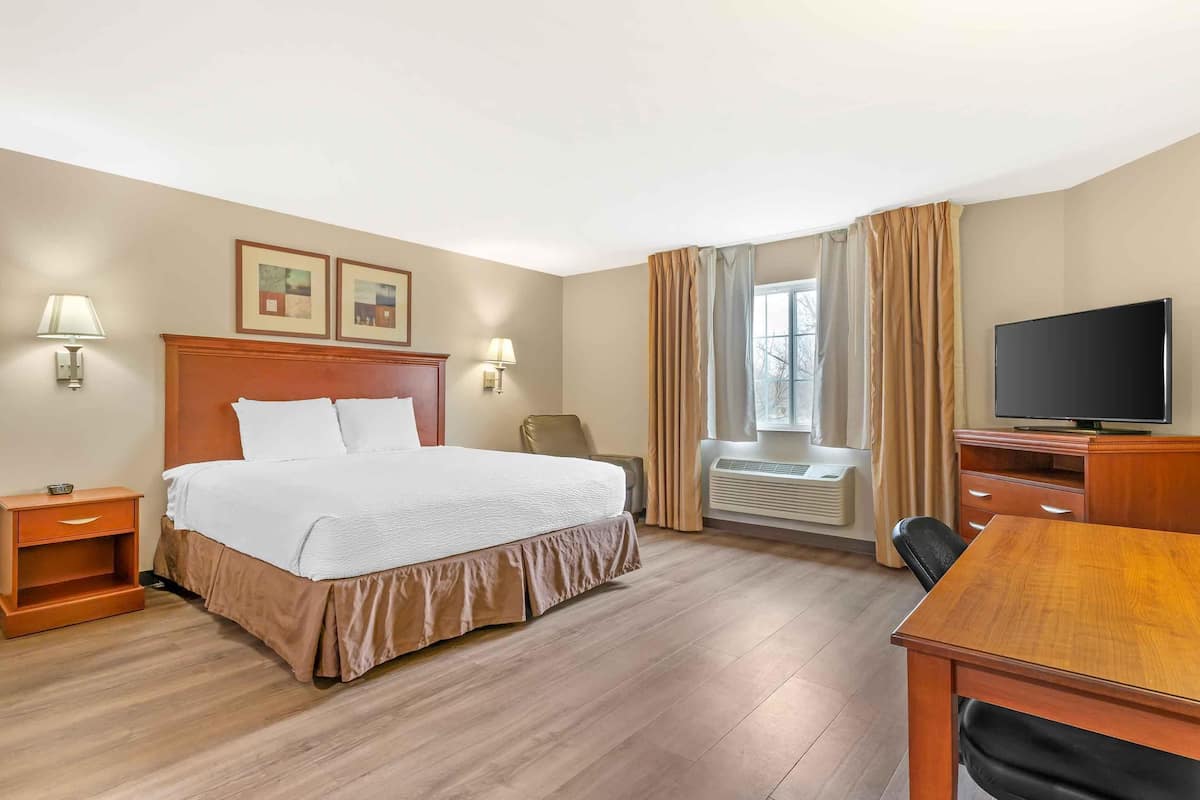 A hotel room with a bed, bedside tables, a desk, a television, and a window with curtains.