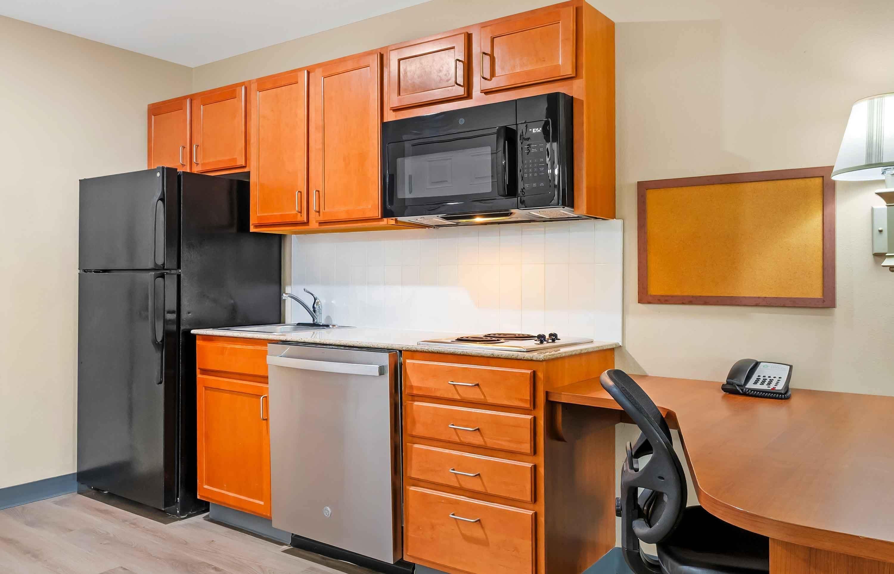 Una cocina compacta con armarios de madera, un refrigerador negro, un microondas, un lavavajillas y una pequeña mesa con un teléfono.