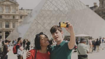 A couple taking a selfie with the Louvre Pyramid in the background.