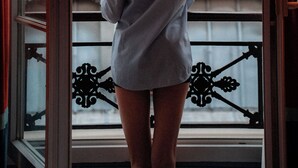 A person standing at a window with a view of buildings outside.
