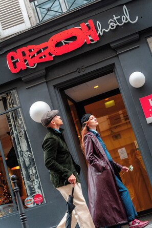 A hotel entrance with a large red sign, a glass door, and a visible number '25' on the wall. - Hotel Crayon  (Paris)