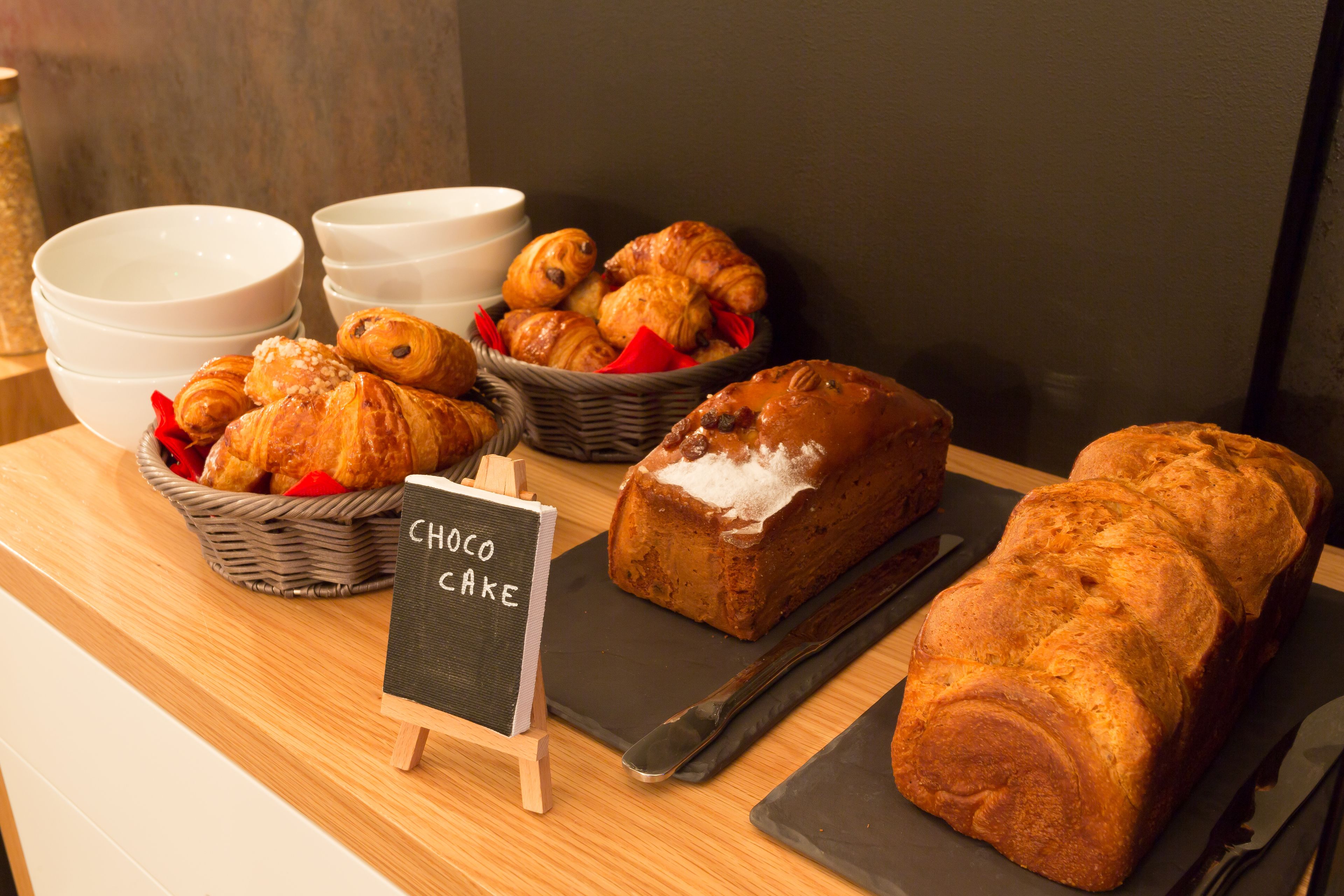 Una exhibición de productos horneados, incluyendo croissants y una hogaza de pastel de chocolate, sobre una mesa de madera.