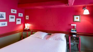 Une chambre d’hôtel avec un lit, des tables de chevet, un bureau et un mur orné de tableaux.