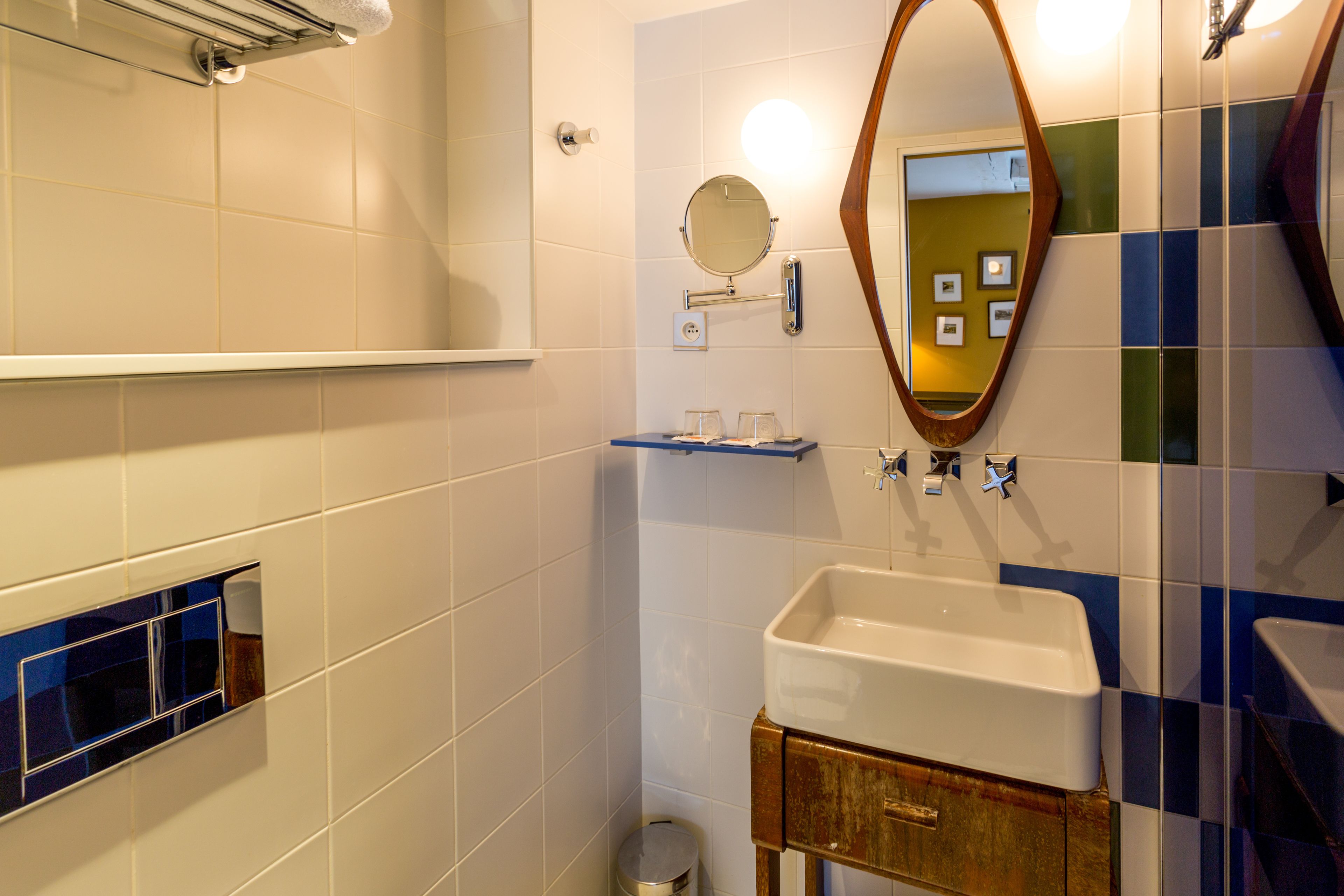 Une salle de bain avec un lavabo blanc, un miroir et une petite étagère sur laquelle sont posés des verres.
