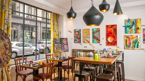 A dining area with wooden tables and chairs, black pendant lights, and colorful artwork on the walls.