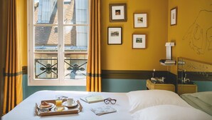 A hotel room with a bed, breakfast tray, framed pictures, and a window with curtains.