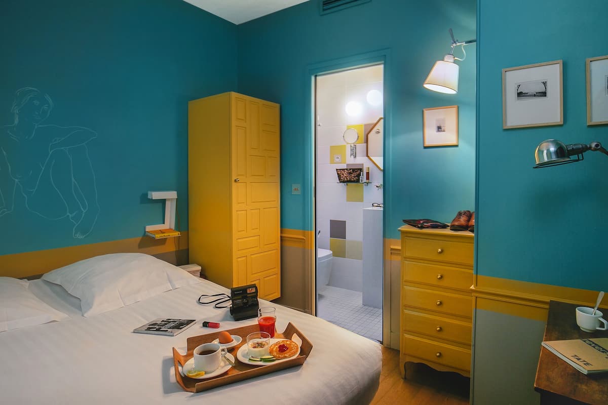 A hotel room with a bed, a tray with breakfast items, a wardrobe, and a bathroom visible through an open door.