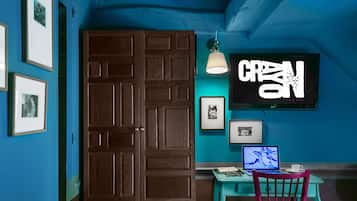 A room with a wooden door, teal walls, a teal desk, a red chair, a TV, and framed pictures.