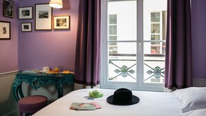 A hotel room with a bed, a table with breakfast items, a hat, and framed pictures on the wall.